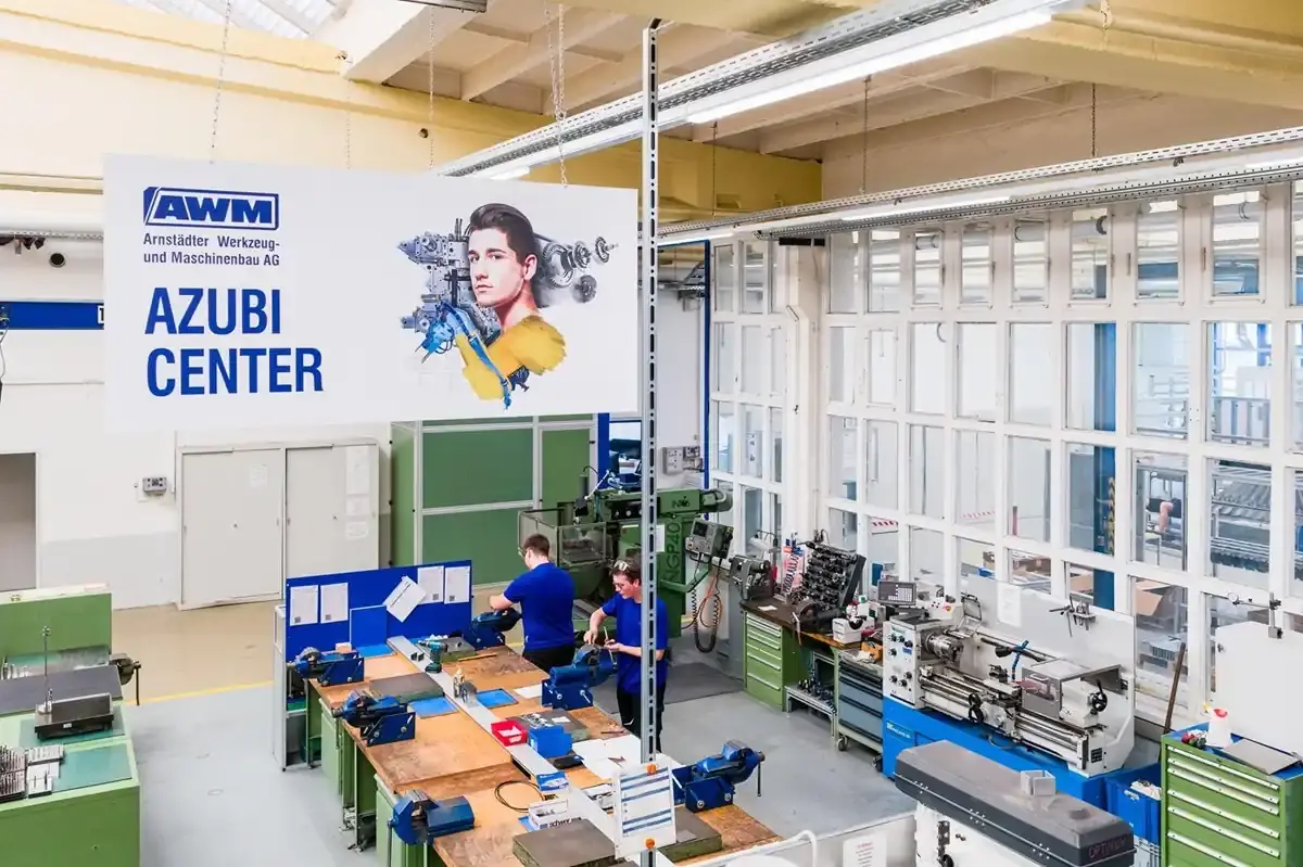 High-angle view of the AWM GmbH AZUBI CENTER showing trainees at workbenches and machines in the modern training workshop for toolmaking and custom machine building.