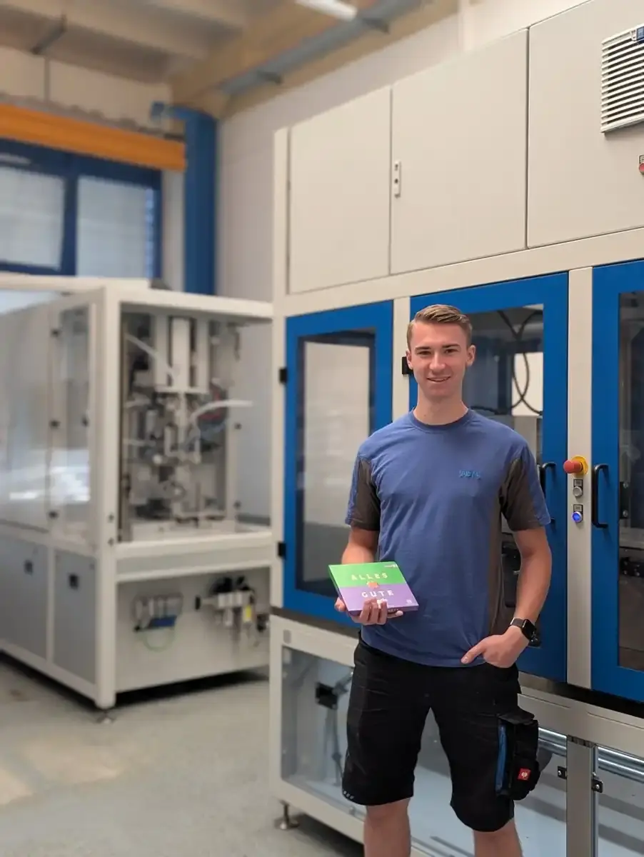 Apprentice training to become a mechatronics technician holding a gift box in the AWM production hall
