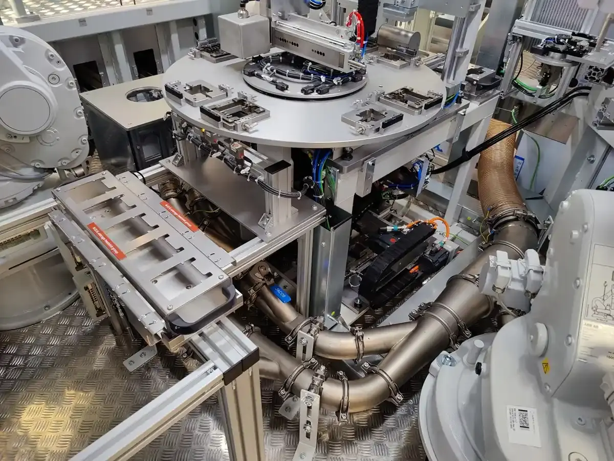 Ansicht eines automatisierten Rundtakt-Drehtischs mit integrierten Absaugrohren, pneumatischen Leitungen und robotergestützten Handhabungsstationen im Sondermaschinenbau bei AWM Arnstadt.