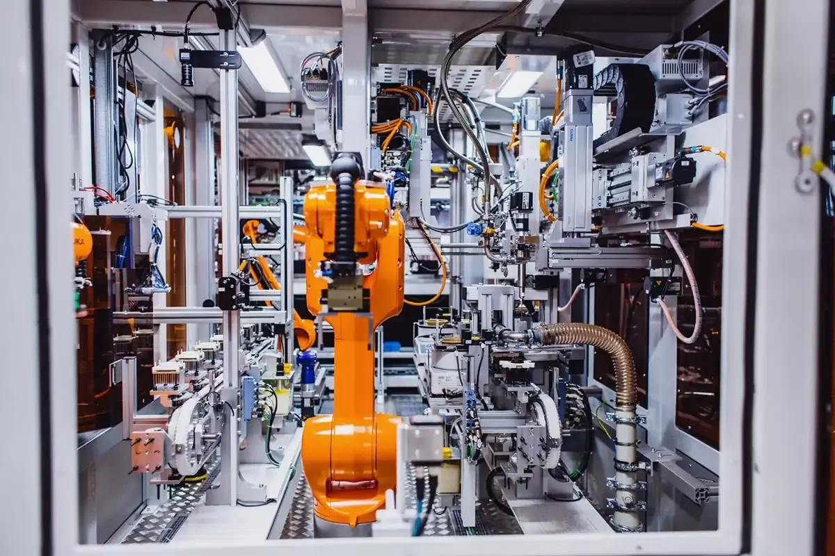 Innenansicht einer vollautomatisierten AWM-Montagezelle mit orangefarbenem KUKA-Industrieroboter, Linearachsen und vernetzter Transportsystem-Technik.